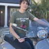 Red Vespa GTS auto scooter on a green t-shirt being modelled by a young man on a grey scooter