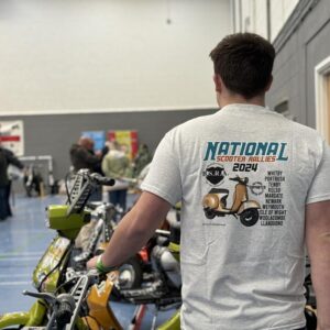 Scooterist sitting on a Vega scooter wearing the 2024 national scooter rallies t-shirt - a view of his back